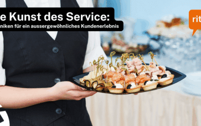 Servicemitarbeiter hält ein Tablett mit kunstvoll angerichteten Häppchen, darunter Lachs, Käse und dekorative Spiesse. Hintergrund zeigt Gläser und Buffet. Text auf dem Bild: ‚Die Kunst des Service: Techniken für ein aussergewöhnliches Kundenerlebnis‘, Logo ritzy*.