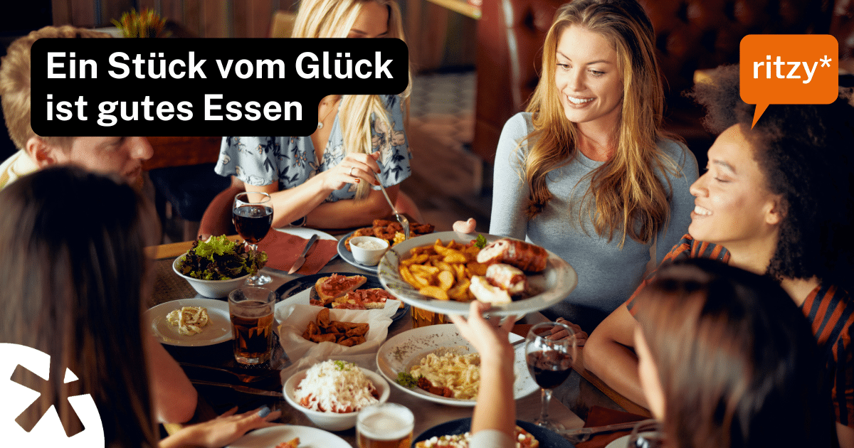 Gruppe von Freunden geniesst gemeinsam ein Restaurant-Essen mit Pommes, Fleischgerichten und Salaten am Tisch, ritzy* Werbebanner „Ein Stück vom Glück ist gutes Essen"